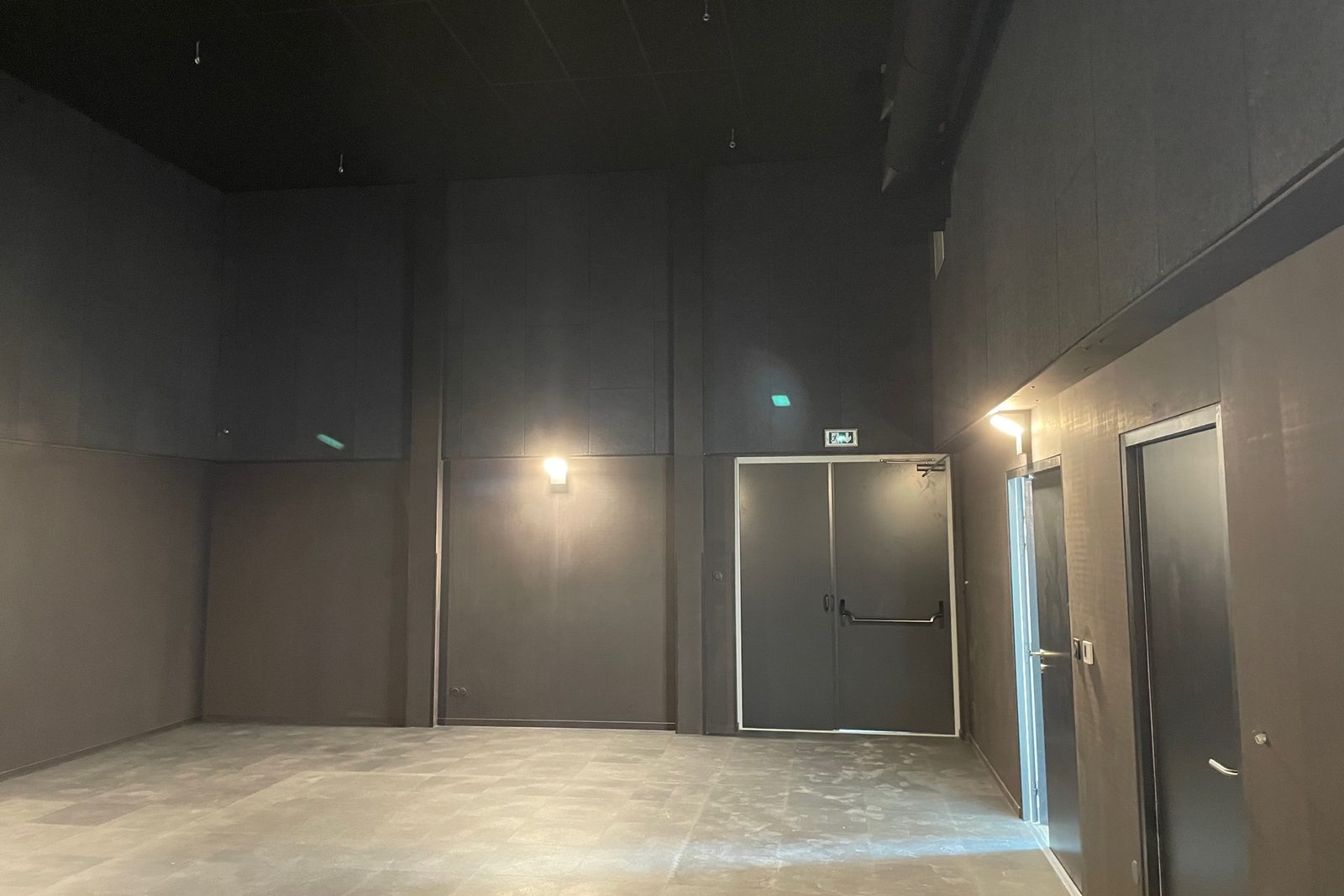 Salle en double hauteur, parois et plafond noirs, issue de secours vers l’extérieur