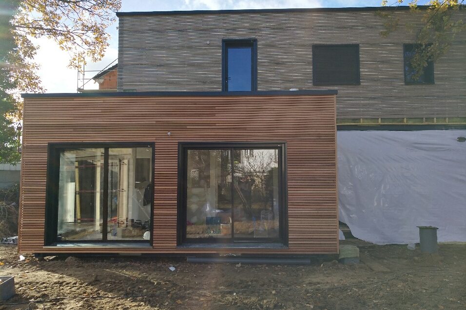 Maison à étage en containers, rez-de-chaussée en bardage bois avec grandes baies et étage en retrait