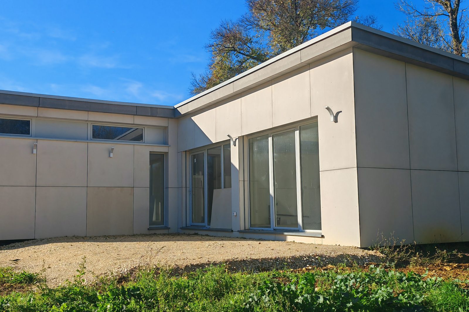 Maison de plain-pied en L en containers, façades en panneaux clairs et grandes baies vitrées